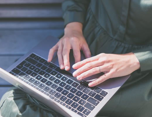 Kvinde der sidder og tager noter på sin computer, mens hun er ved at tage en online uddannelse