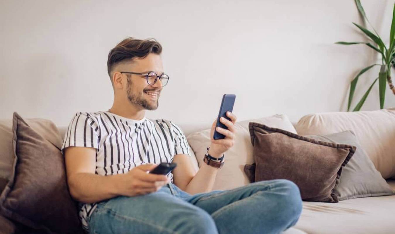 Mand, der sidder i sin sofa og ser undervisningen, fra en online uddannelse, på sin smartphone 