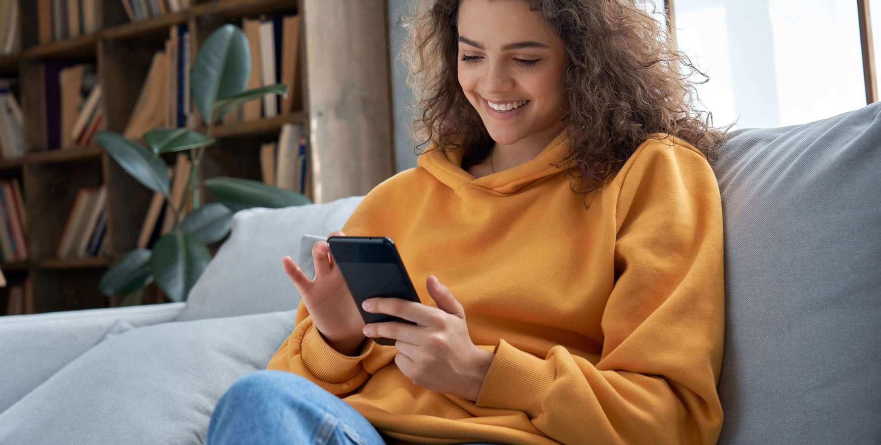 Kvinde, der sidder i sin sofa med sin smartphone og tager en online uddannelse