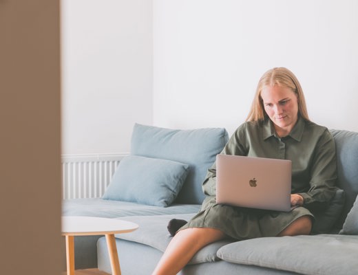 Kvinde, der sidder i sin sofa med computer og ser undervisningen fra en online uddannelse