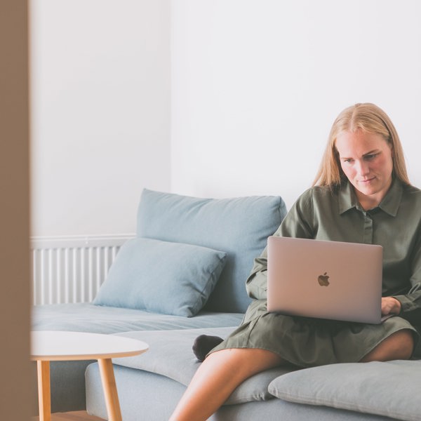 Kvinde, der sidder i sin sofa med computer og ser undervisningen fra en online uddannelse